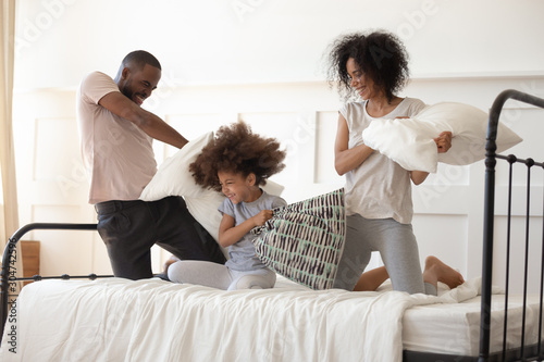 Happy biracial family with daughter have pillow fight in bedroom