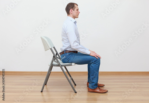 caucasian man sitting on the edge of chair in correct  posture