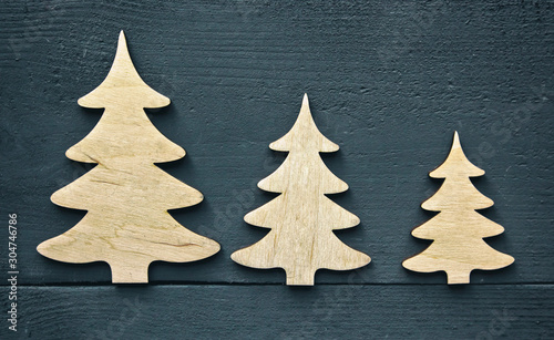 The beautiful christmas background with three small wooden decorations on the dark wooden desk.