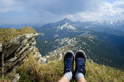 Young traveller relaxing on top of the mountain range during hiking. Hiker shoes on background of panoramic mountains landscape view. Carpathians, Ukraine.