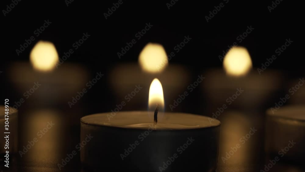 The candle is slowly burning in the darkness on the background of three lights The candle is slowly burning in the darkness on the background of three lights