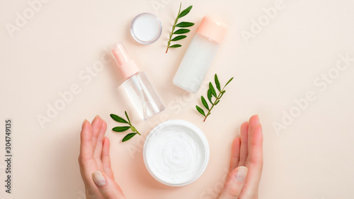 Jar of organic hand cream, essential oils bottle and green leaves on beige background. Skin care, organic natural beauty products concept