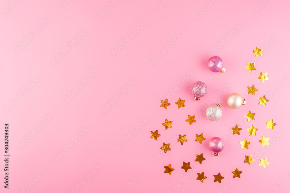 Gold stars and shiny christmas toys are scattered on a pink pastel background.