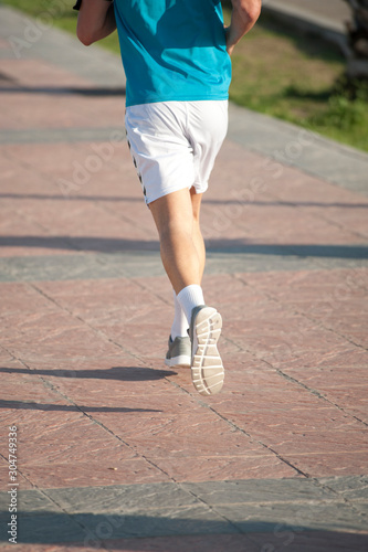 runner with blue t-shirt and white short sports pants white socks and gray sneakers both feet in the air