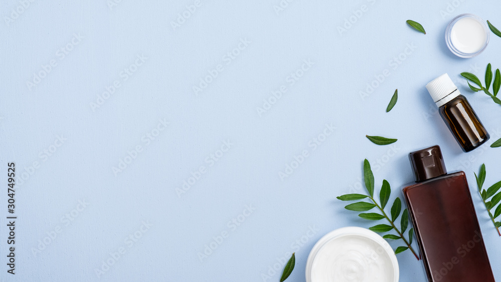 Flat lay composition with organic cosmetic products on blue background with copy space. Top view essential oil, lotion, cream jar and green leaves. Natural organic beauty product concept. - obrazy, fototapety, plakaty 