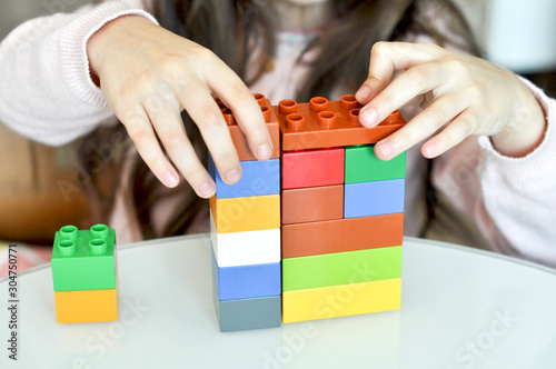 Child playing with plastic colorful blocks constructor at kindergarten. Close up of little girl hands building with colorful construction at home. Little girl with educational toys blocks at preschool photo