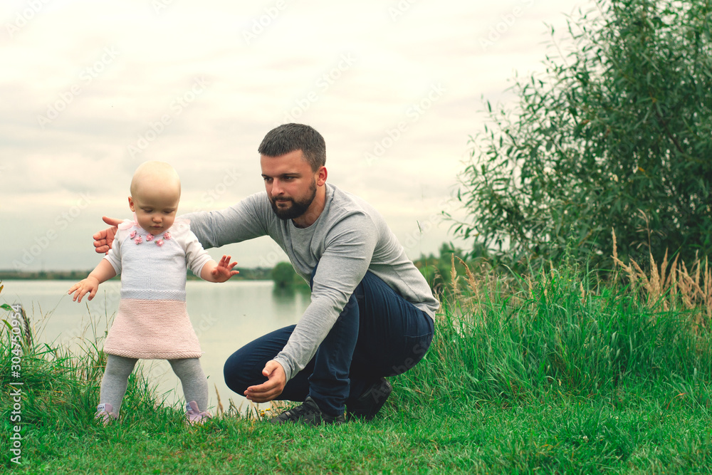 Dad teaches daughter to walk, park, nature. Walk on the grass. Father and daughter. First steps. Dad teaches daughter to walk, park, nature. Walk on the grass. Father and daughter. First steps.