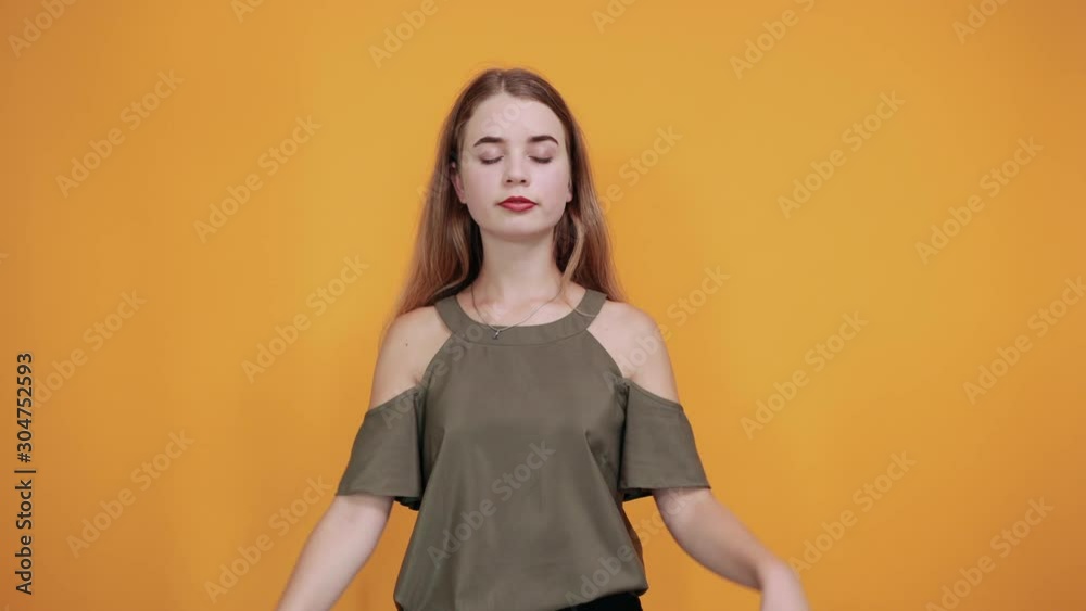 Portrait of smiling joyful pretty young woman in casual clothes standing with closed eyes, doing yoga sing isolated on orange wall background in studio. People sincere emotions lifestyle concept. Portrait of smiling joyful pretty young woman in casual clothes standing with closed eyes, doing yoga sing isolated on orange wall background in studio. People sincere emotions lifestyle concept.