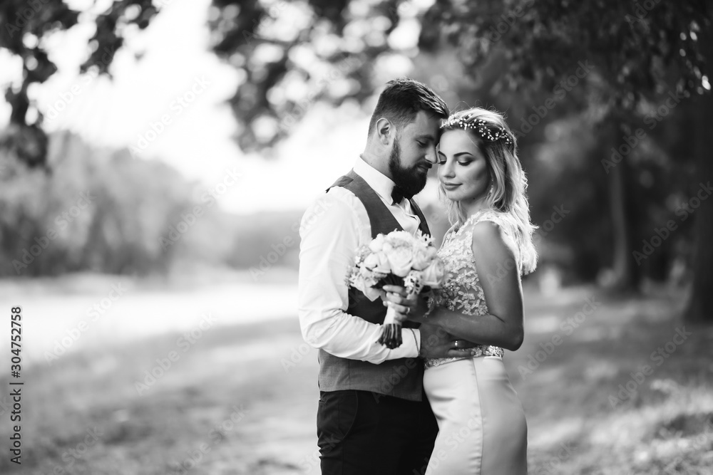 Sensual Black and white foto of bride and groom. Stylish couple of happy newlyweds posing and kisses in the park on their wedding day. Together. The concept of youth, love, fashion and lifestyle. Sensual Black and white foto of bride and groom. Stylish couple of happy newlyweds posing and kisses in the park on their wedding day. Together. The concept of youth, love, fashion and lifestyle.