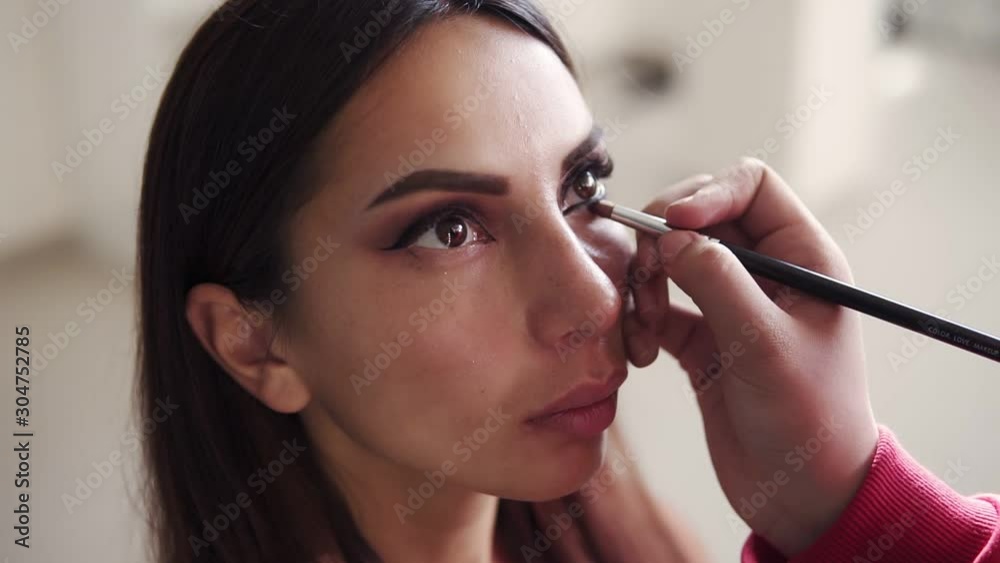 Professional make up in artistic studio. Unrecognizable female make up artist applying and blending model's lower eyelid with eyeshadows. Process of creating flawless smokey eyes make up look