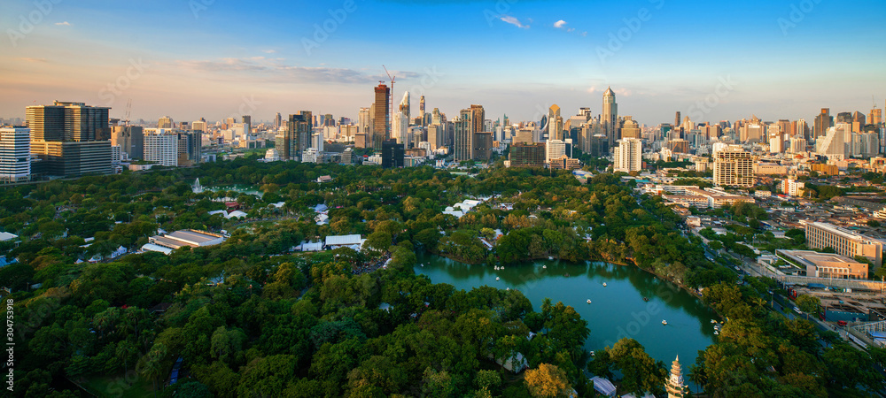 Naklejka premium Zwiedzanie parku Lumpini wokół nowoczesnych biurowców i kondominium w centrum Bangkoku z chmurami o zachodzie słońca