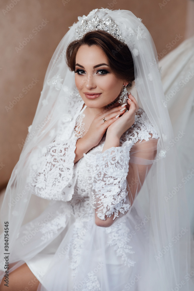Bride wedding morning. Fashion bride gorgeous beauty, bride woman in robe. Bride touches earrings. Portrait wedding makeup and hairstyle, girl with veil and jewelry at home. Bride wedding morning. Fashion bride gorgeous beauty, bride woman in robe. Bride touches earrings. Portrait wedding makeup and hairstyle, girl with veil and jewelry at home.