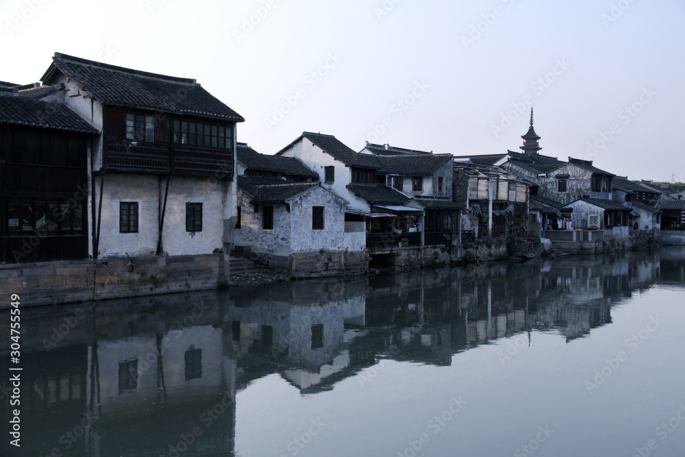 The ancient houses in Jiangsu, China, the white walls and black corrugated are scattered next to the canal. In the early morning, the light of the river reflects the ancient scenery of the river.