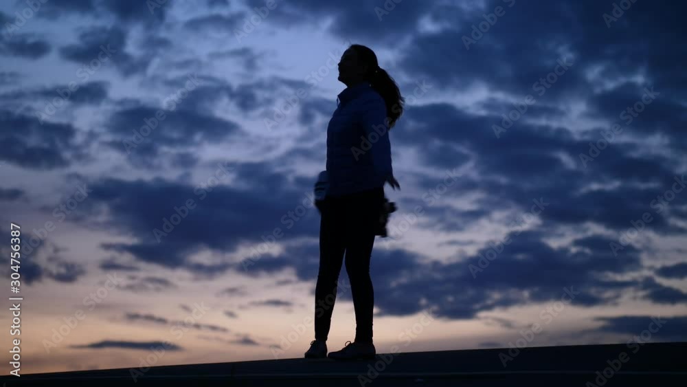 Cheery traveller woman turn around light suitcase, silhouetted shot against dark clouds. Tourist wearing autumn clothes, happy or celebrate something Cheery traveller woman turn around light suitcase, silhouetted shot against dark clouds. Tourist wearing autumn clothes, happy or celebrate something