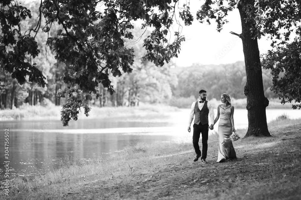 Sensual Black and white foto of bride and groom. Stylish couple of happy newlyweds posing in the park on their wedding day. Handsome bearded groom admires and kisses pretty bride. Together. Sensual Black and white foto of bride and groom. Stylish couple of happy newlyweds posing in the park on their wedding day. Handsome bearded groom admires and kisses pretty bride. Together.
