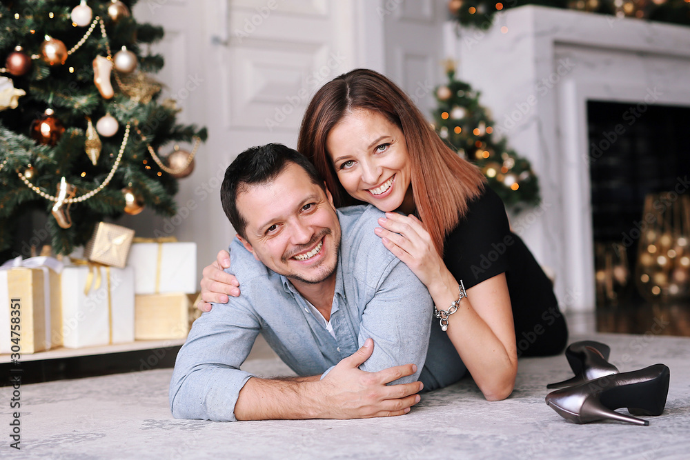 Beautiful young couple next to the Christmas tree. A young woman and a man are smiling and having fun together. Beautiful young couple next to the Christmas tree. A young woman and a man are smiling and having fun together.