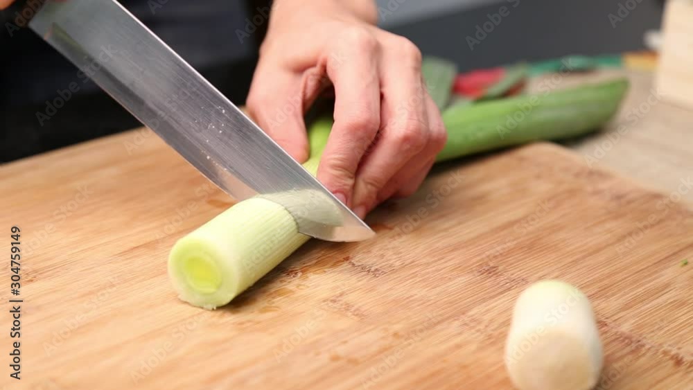 Female hand cutting leek on a wooden board Female hand cutting leek on a wooden board