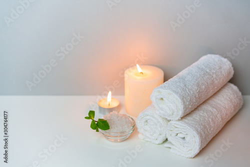 SPA treatments concept photo on grey background with stack of white towels, candles and cup of sea salt.