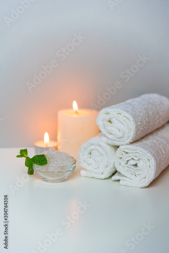 Stack of white towels, candles light, sea salt prepared for salon procedure. Natural health & SPA concept photo, vertical orientation. 