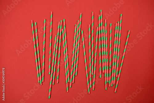 Red and green striped straws on red background, copy space. Christmas texture. Minimalism concept. Top view, flat lay