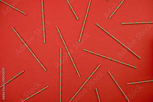 Red and green striped straws on red background, copy space. Christmas texture. Minimalism concept. Top view, flat lay