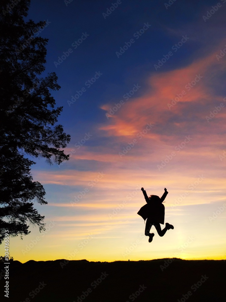 silhouette of woman jumping on sunset background of blue sky