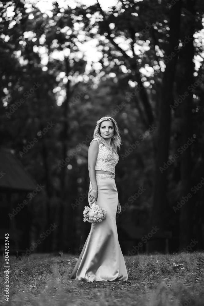 Black and white foto of beautiful bride with a wedding bouquet for a walk in the park. Happy newlywed woman stands among green bushes in the garden. Smiling bride. Wedding day. Fashion bride. Black and white foto of beautiful bride with a wedding bouquet for a walk in the park. Happy newlywed woman stands among green bushes in the garden. Smiling bride. Wedding day. Fashion bride.