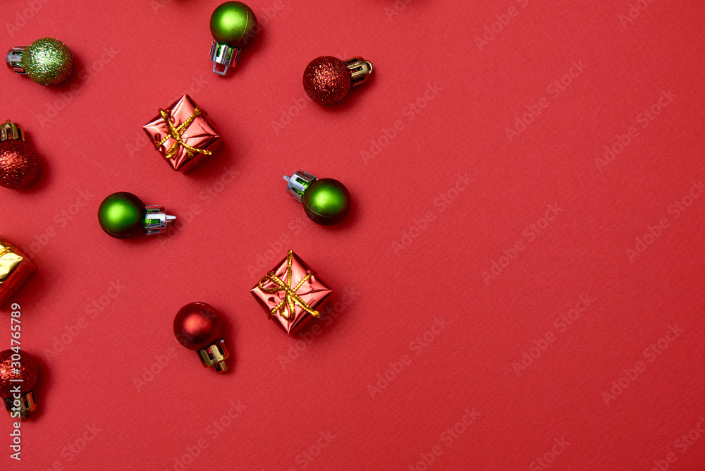 Creative Christmas pattern with red and green shiny baubles and gifts on red background, copy space. Minimal, winter, new year concept. Top view, flat lay