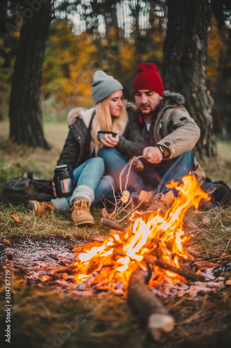 Traveler couple camping and roasting marshmallows over the fire in the forest after a hard day. Concept of trekking, adventure and seasonal vacation.