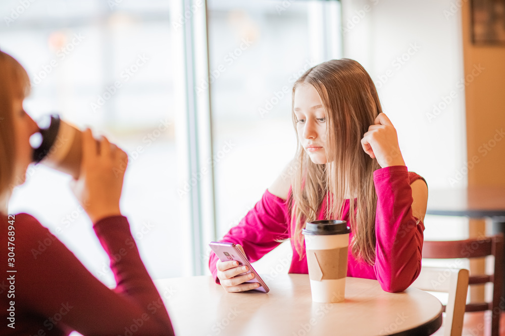 Obraz premium beautiful, sad, serious teenager girls, sitting in cafe have conversation and chatting on mobile phone 