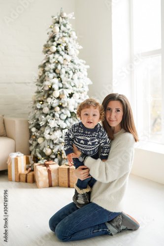 family, winter holidays and people concept - happy mother and baby boy near christmas tree at home