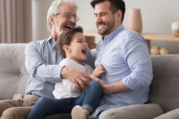 Happy grandfather and father tickling little boy, having fun