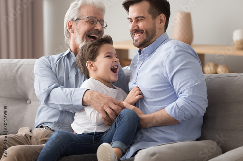 Happy grandfather and father tickling little boy, having fun photo
