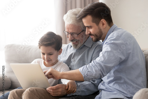 Happy grandfather and father teaching little boy to use laptop