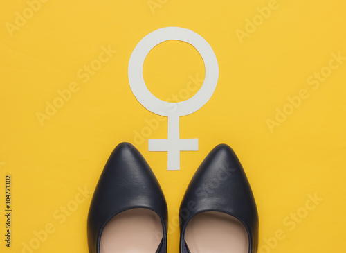 Feminism. Female gender symbol, high heel shoes on yellow background. Top view photo