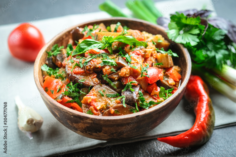 Vegetable saute or caponata, or pisto with eggplant, peppers, tomatoes and herbs in rustic bowl on a dark background. Vegetable saute or caponata, or pisto with eggplant, peppers, tomatoes and herbs in rustic bowl on a dark background.