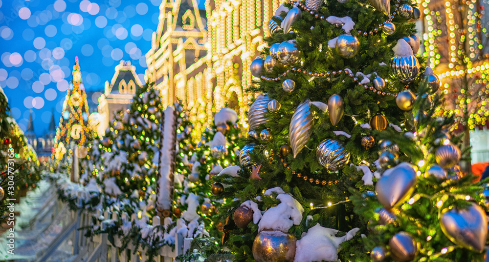 Fototapeta premium Stylish garland lights on christmas trees fir branches with christmas decorations at front of a building at european city street. Festive street decor in winter holidays