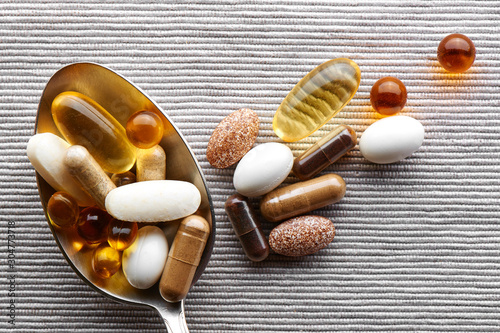 Close-up tablespoon filled with various dietary supplements, tablets and vitamins on a gray fabric background photo