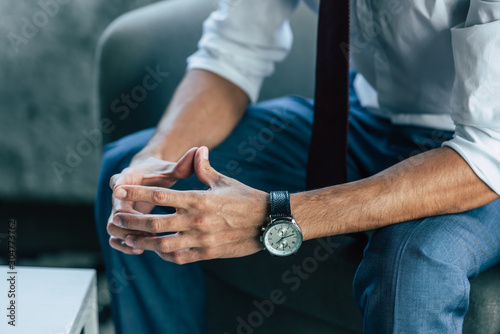 cropped view of businessman sitting in armchair with folded hands