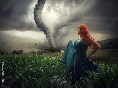 Beautiful female standing on a field with a tornado in the background captured in the storm