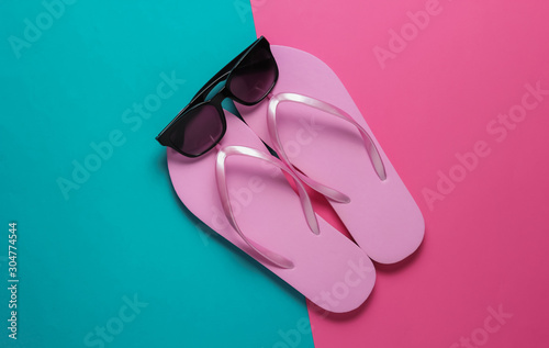 Summer beach concept. Sunglasses, flip flops on pink blue background. Top view