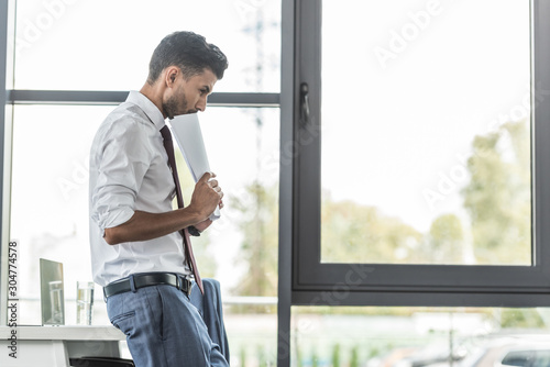 thoughtful businessman holding documents while standing at workplace Free Download thoughtful businessman holding documents while standing at workplace - GFXLoad