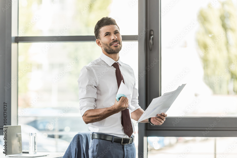 Fototapeta premium upset businessman holding documents and crumpling paper while looking away in office