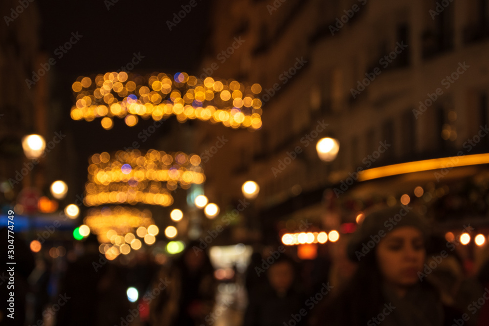 Blurry photo of Montorgueil street in Paris at night  with beautiful Christmas lights decoration and unrecognizable crowd. Winter holidays vacation and travel concept. Festive urban blurry background.