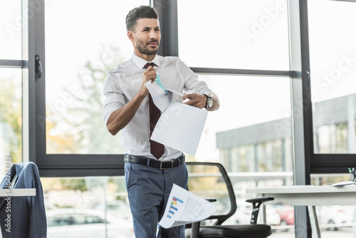 Φωτογραφία displeased businessman tearing documents and looking away while standing near wi