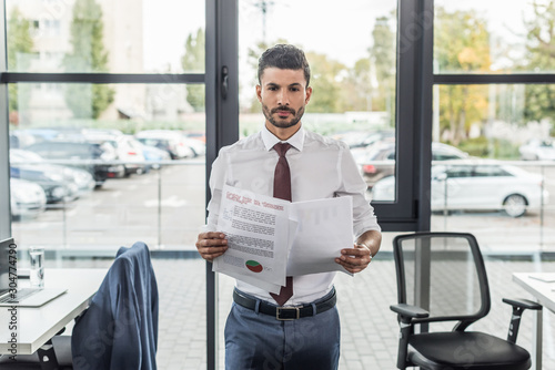 discouraged businessman looking at camera while holding documents