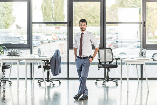 young, confident businessman standing in modern office and looking at camera