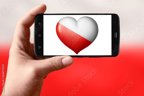 Poland flag in a heart shape on the screen. Smartphone in hand shows a flag heart. photo