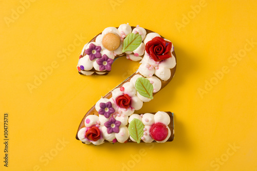 Number two cake decorated with flowers and macarons isolated on yellow background