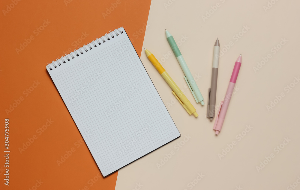 A lot of colored pens with notebook close-up on brown beige background. Top view A lot of colored pens with notebook close-up on brown beige background. Top view
